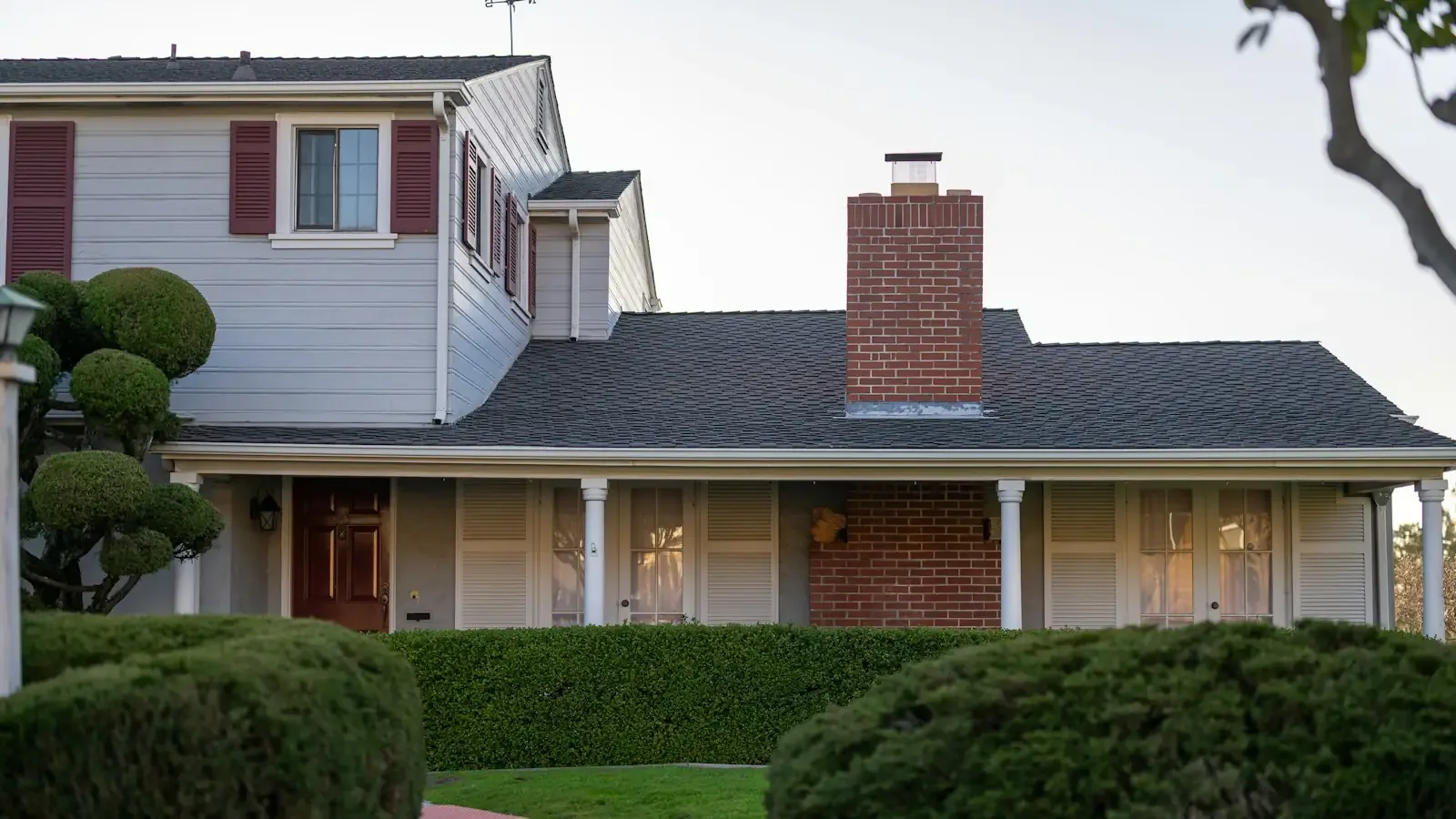 An older white house with a brick chimney and red shutters