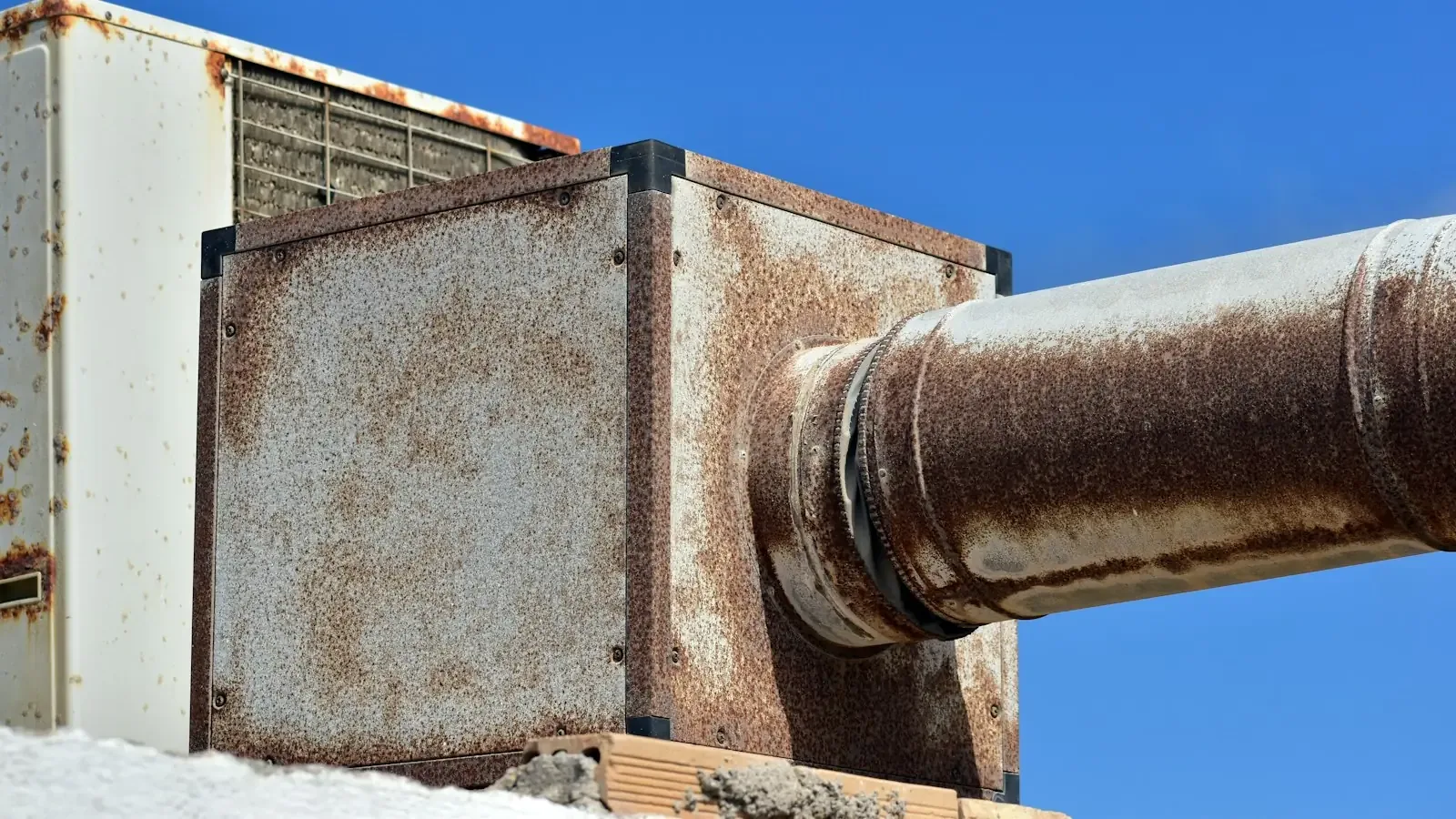 A rusted metal pipe running out of an old steel box against a blue sky